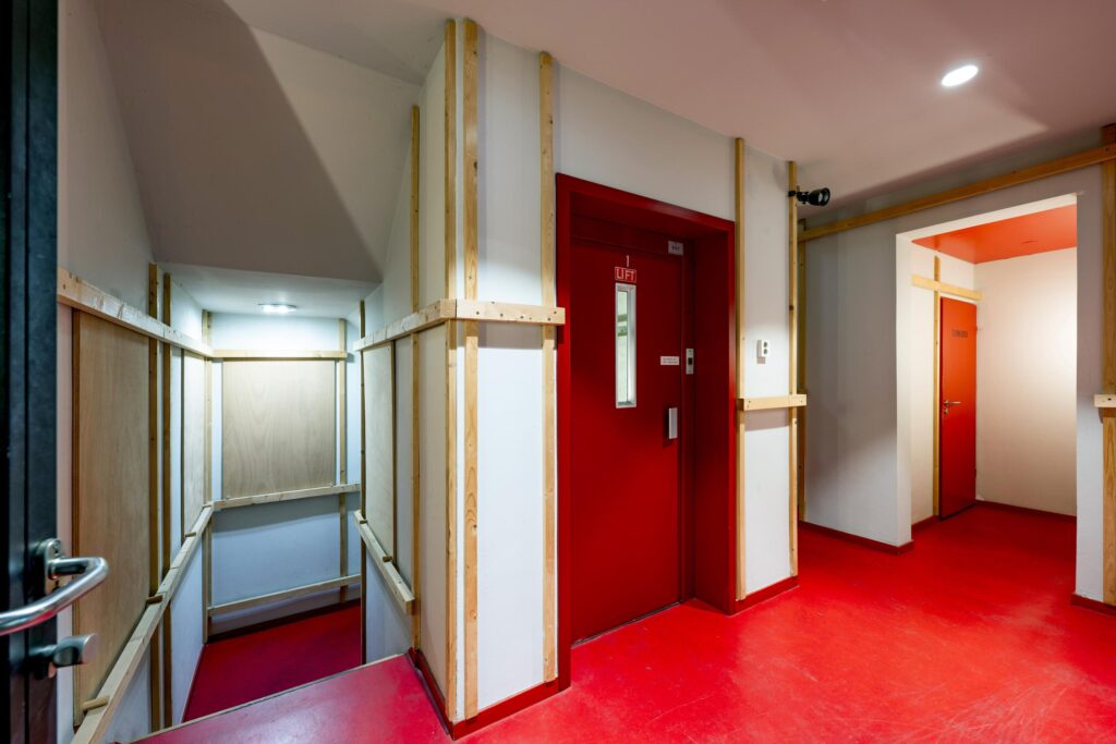 Hal met felrode vloer en deuren, inclusief liftdeur en trap bij De Ruijterkade.